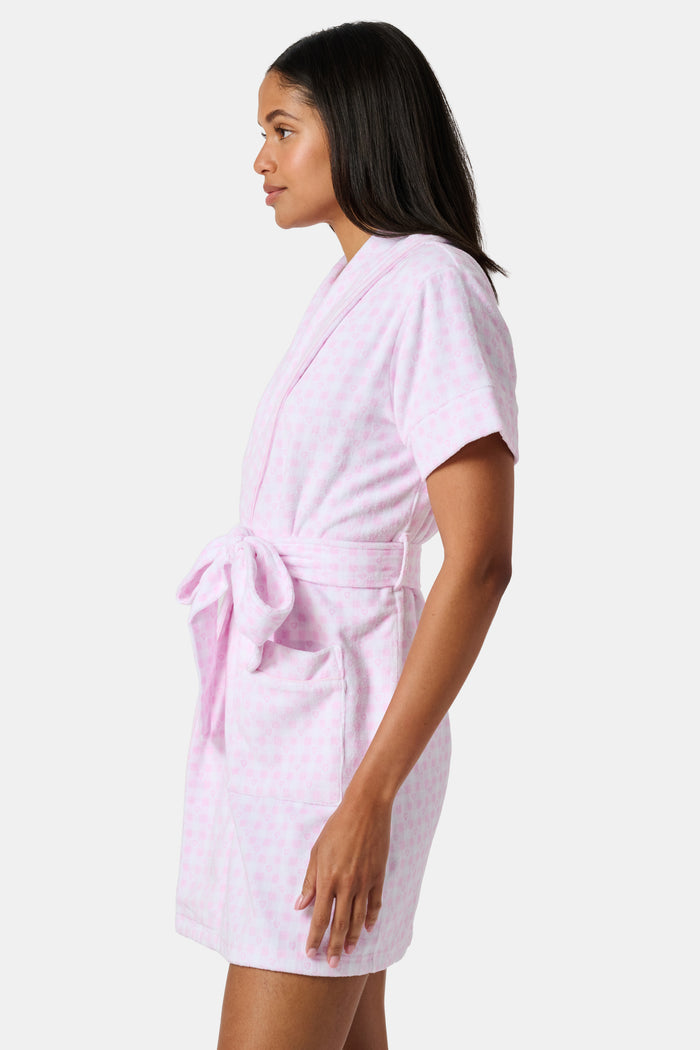 The Roller Rabbit Gingham Hearts Brooks Robe features a light pink gingham pattern with subtle hearts, crafted from soft cotton. This short-sleeve robe includes front pockets and a matching waist tie, and is displayed against a plain white background.