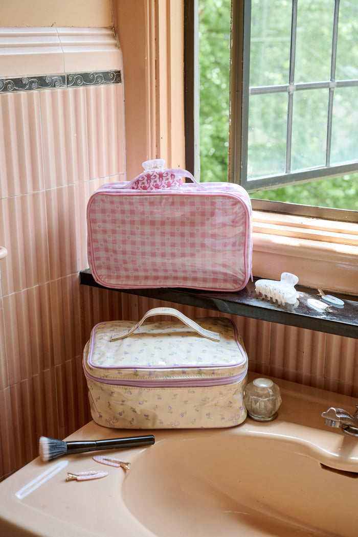 The Roller Rabbit Gingham Hearts Hanging Toiletry Case is a rectangular travel bag featuring pink and white gingham checks adorned with small heart patterns and a top handle, displayed against a plain white background.