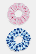 The Roller Rabbit Gingham Hearts Scrunchie Set Of 2 features one pink and white gingham scrunchie with small hearts and one blue and white gingham scrunchie with small hearts, displayed vertically on a plain background.