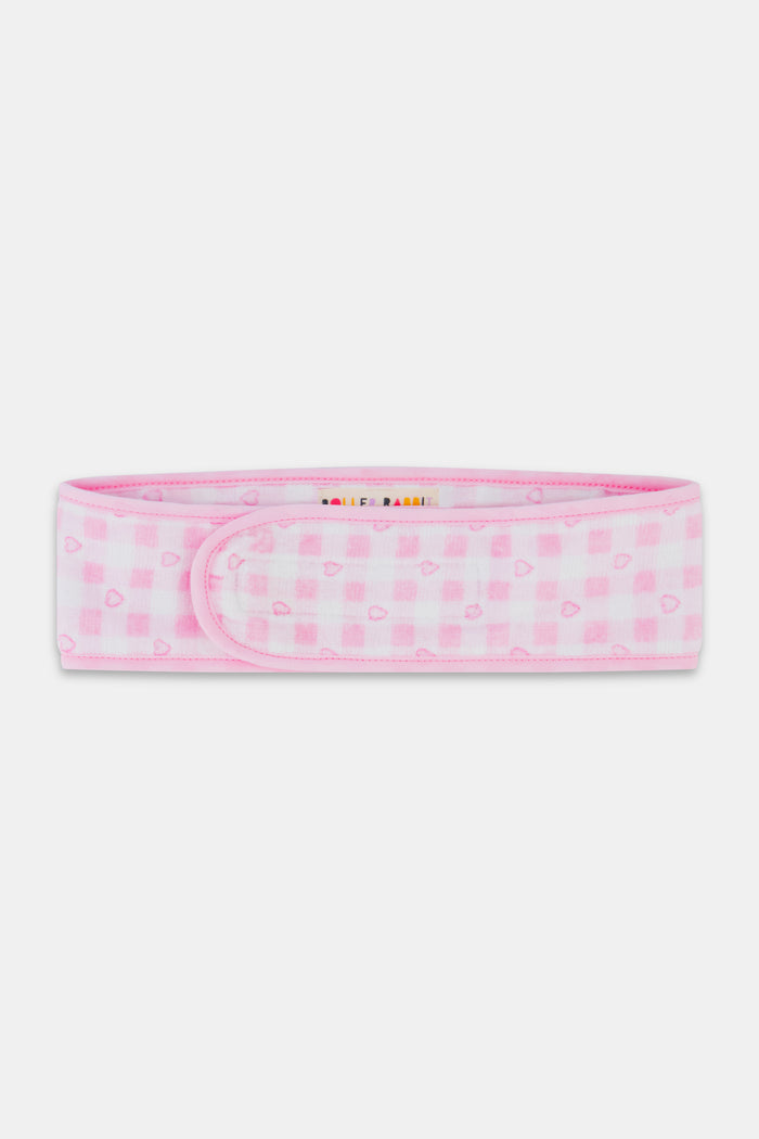 The Roller Rabbit Gingham Hearts Spa Headband is crafted from 100 cotton terrycloth and showcases a pink and white checkered pattern accented with small hearts. It features a convenient hook-and-loop fastener and is displayed laid flat on a white background.