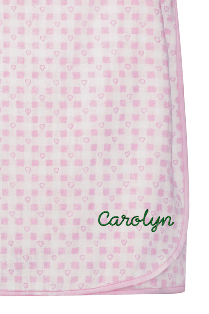The Roller Rabbit Gingham Hearts Spa Headband is crafted from 100 cotton terrycloth and showcases a pink and white checkered pattern accented with small hearts. It features a convenient hook-and-loop fastener and is displayed laid flat on a white background.