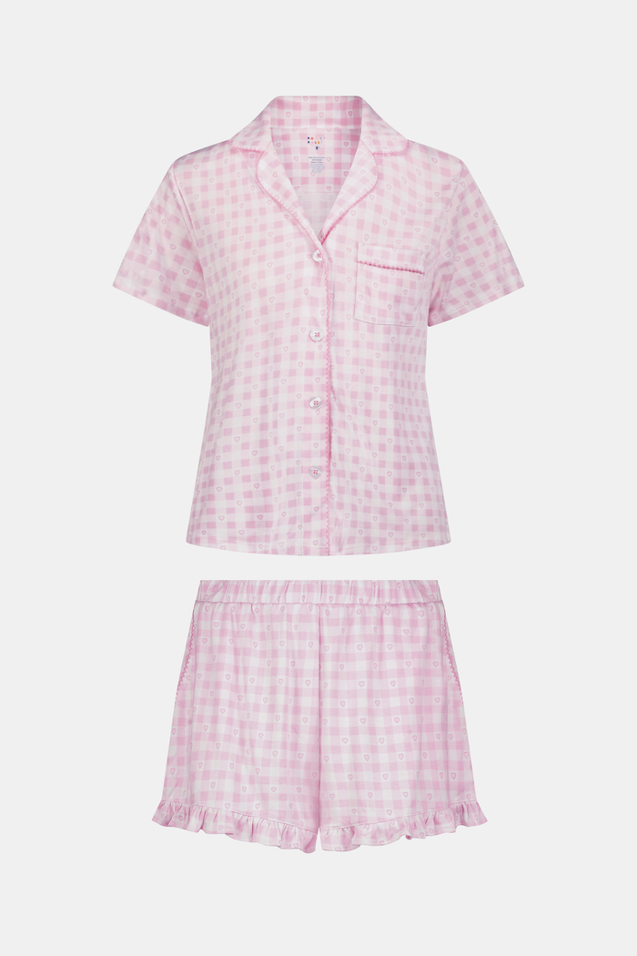 The Gingham Hearts Wyatt Polo Pajamas by Roller Rabbit are a pink and white gingham short-sleeve pajama set, featuring a button-up shirt with chest pocket and matching shorts with a ruffled hem, all crafted from soft Pima cotton. This set is shown on a white background.