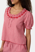 A woman wears the Roller Rabbit Gingham Quincy Top, a cotton blouse with puffed sleeves and red embroidery at the neckline. Only her upper body is visible.