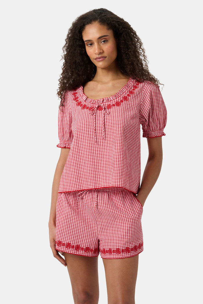 A woman wears the Roller Rabbit Gingham Quincy Top, a cotton blouse with puffed sleeves and red embroidery at the neckline. Only her upper body is visible.