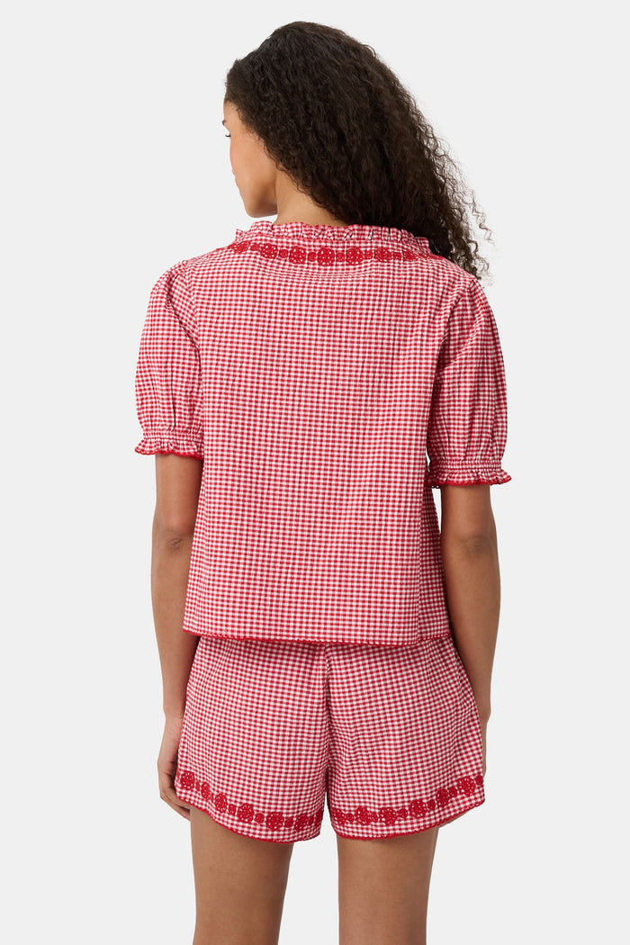 A woman wears the Roller Rabbit Gingham Quincy Top, a cotton blouse with puffed sleeves and red embroidery at the neckline. Only her upper body is visible.