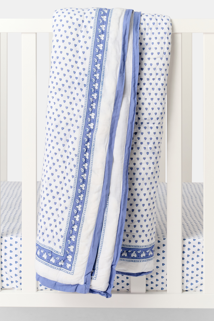 The Hearts Baby Quilt by Roller Rabbit is a folded white cotton quilt with blue and purple geometric borders, adorned with small heart prints—perfect for baby bedding.