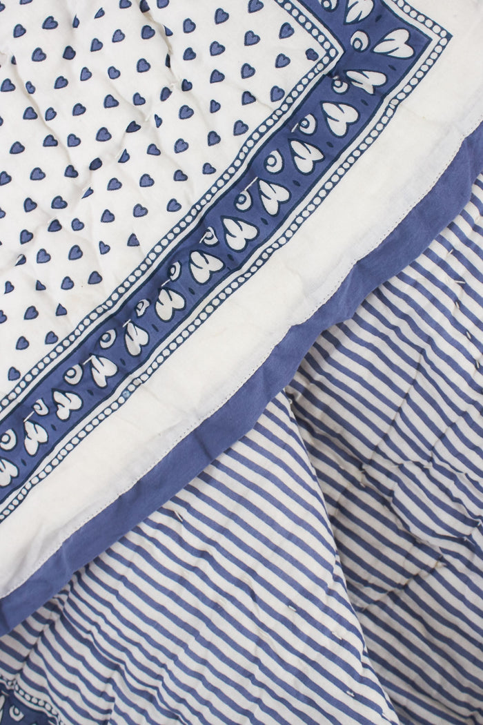 The Hearts Baby Quilt by Roller Rabbit is a folded white cotton quilt with blue and purple geometric borders, adorned with small heart prints—perfect for baby bedding.