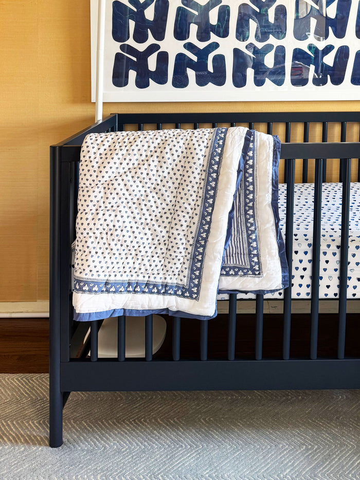 The Hearts Baby Quilt by Roller Rabbit is a folded white cotton quilt with blue and purple geometric borders, adorned with small heart prints—perfect for baby bedding.