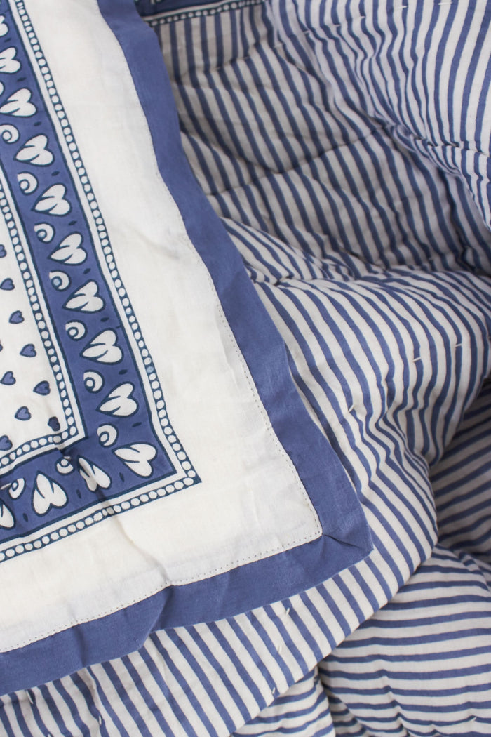 The Hearts Baby Quilt by Roller Rabbit is a folded white cotton quilt with blue and purple geometric borders, adorned with small heart prints—perfect for baby bedding.