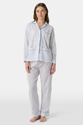 A person stands barefoot in Roller Rabbit’s Hearts Loungewear, a matching cotton pajama set with heart prints, featuring a button-up long sleeve top and long pants. The background is plain white.