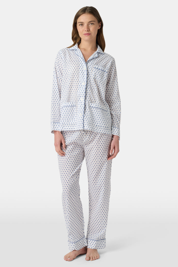 A person stands barefoot in Roller Rabbit’s Hearts Loungewear, a matching cotton pajama set with heart prints, featuring a button-up long sleeve top and long pants. The background is plain white.