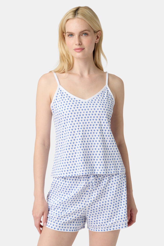 A woman wears the Roller Rabbit Hearts Mischa Set, a Pima cotton loungewear set with a white base and blue hearts. The set includes a sleeveless camisole top and shorts, styled against a plain light background.