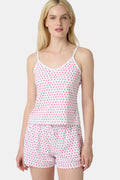 A woman wears the Roller Rabbit Hearts Mischa Set, a matching white loungewear set with pink hearts, featuring a sleeveless camisole and shorts made from soft Pima Cotton, standing against a plain white background.