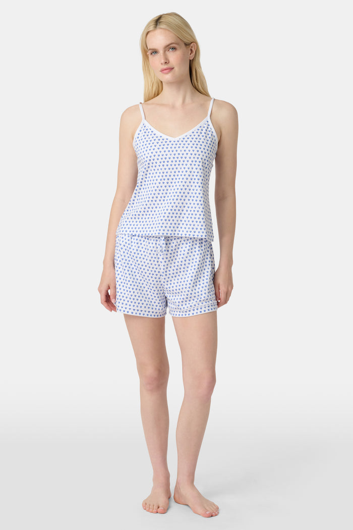 A woman wears the Roller Rabbit Hearts Mischa Set, a Pima cotton loungewear set with a white base and blue hearts. The set includes a sleeveless camisole top and shorts, styled against a plain light background.