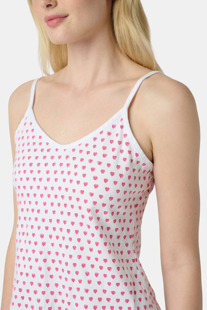 A woman wears the Roller Rabbit Hearts Mischa Set, a matching white loungewear set with pink hearts, featuring a sleeveless camisole and shorts made from soft Pima Cotton, standing against a plain white background.