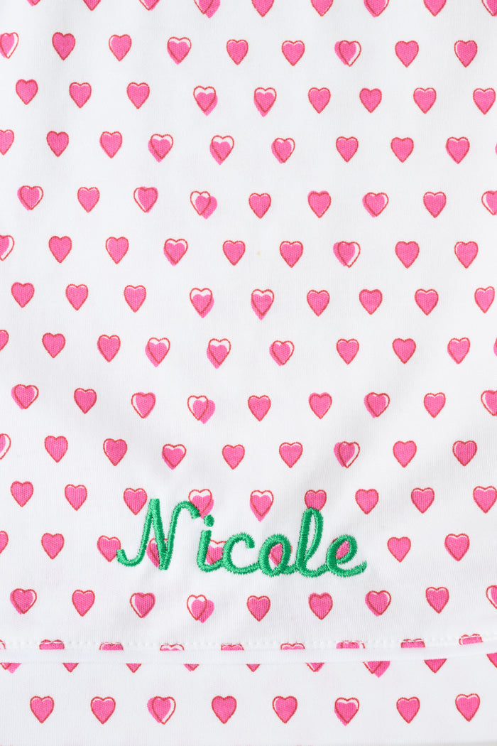 A woman wears the Roller Rabbit Hearts Mischa Set, a matching white loungewear set with pink hearts, featuring a sleeveless camisole and shorts made from soft Pima Cotton, standing against a plain white background.