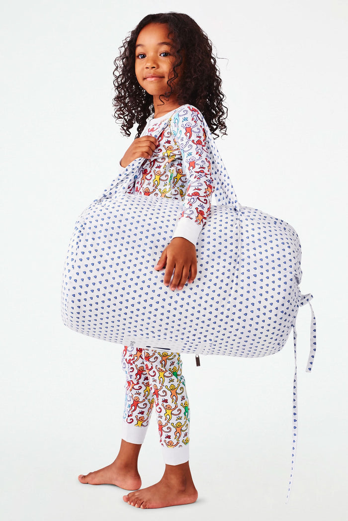 The Roller Rabbit Hearts Sleepover Bag is a large white bag with small blue hearts, a drawstring top, an external zippered pocket with two blue exclamation points, and "sleepover" printed below. Ideal for carrying kids' sleeping bags.