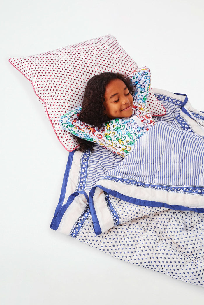 The Roller Rabbit Hearts Sleepover Bag is a large white bag with small blue hearts, a drawstring top, an external zippered pocket with two blue exclamation points, and "sleepover" printed below. Ideal for carrying kids' sleeping bags.