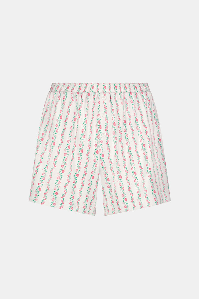 A person wears the Roller Rabbit Hearts Vine Brooklyn Boxer—matching long-sleeve, button-up pajama top and shorts with a pink, green, and white floral stripe pattern—standing against a white background.