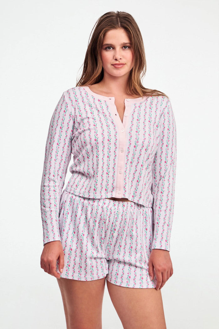 A person wears the Roller Rabbit Hearts Vine Brooklyn Boxer—matching long-sleeve, button-up pajama top and shorts with a pink, green, and white floral stripe pattern—standing against a white background.