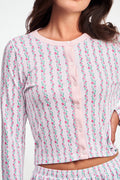 A woman wears the Roller Rabbit Hearts Vine Nessa Cardigan, a pink long-sleeve pima cotton sweater with small green and pink floral vine print and white front buttons. Her hand is on her hip, her face partially out of frame.