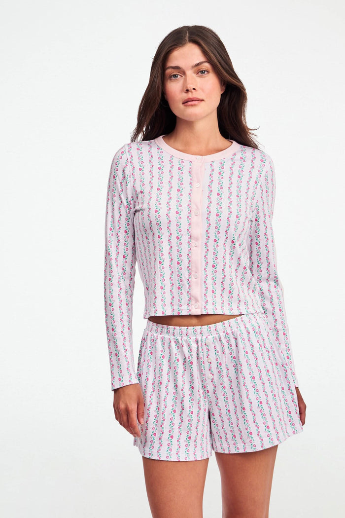 A woman wears the Roller Rabbit Hearts Vine Nessa Cardigan, a pink long-sleeve pima cotton sweater with small green and pink floral vine print and white front buttons. Her hand is on her hip, her face partially out of frame.