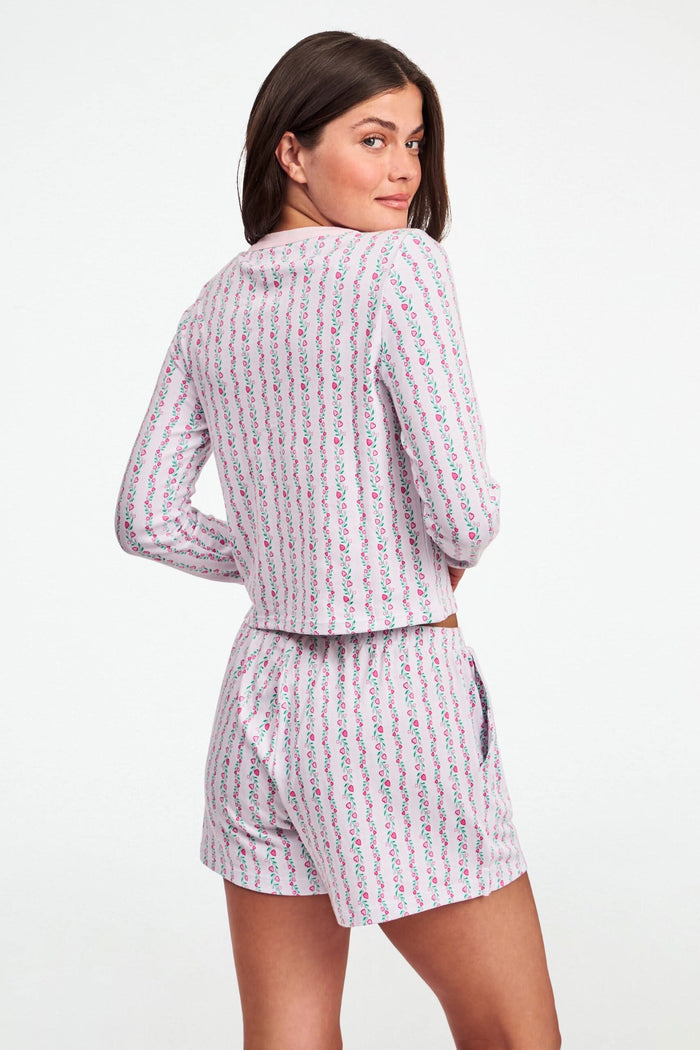 A woman wears the Roller Rabbit Hearts Vine Nessa Cardigan, a pink long-sleeve pima cotton sweater with small green and pink floral vine print and white front buttons. Her hand is on her hip, her face partially out of frame.