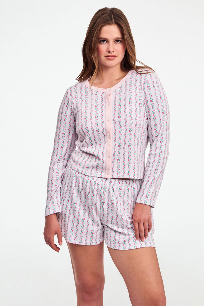 A woman wears the Roller Rabbit Hearts Vine Nessa Cardigan, a pink long-sleeve pima cotton sweater with small green and pink floral vine print and white front buttons. Her hand is on her hip, her face partially out of frame.
