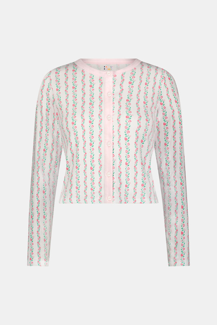 A woman wears the Roller Rabbit Hearts Vine Nessa Cardigan, a pink long-sleeve pima cotton sweater with small green and pink floral vine print and white front buttons. Her hand is on her hip, her face partially out of frame.