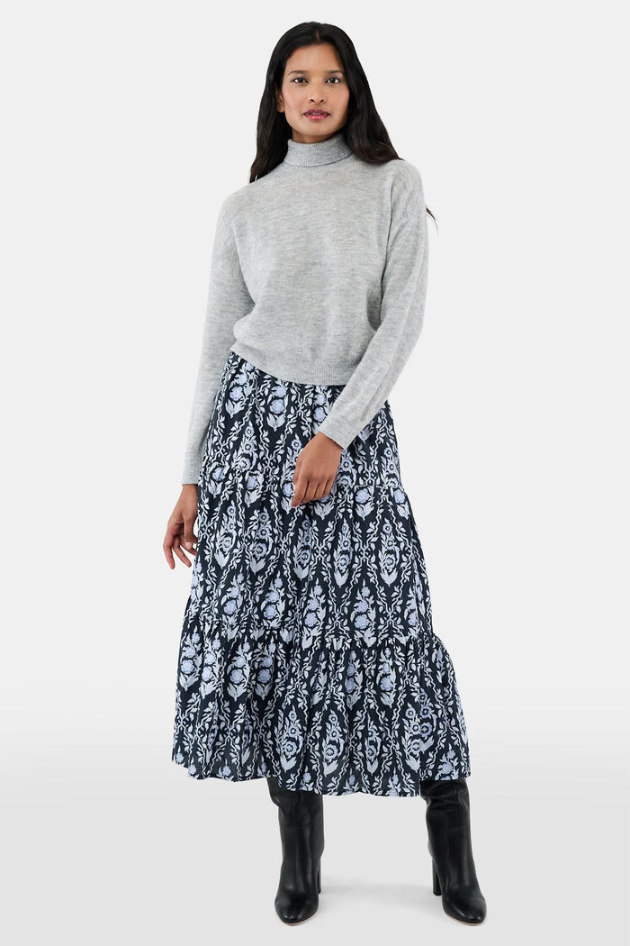 A woman with long dark hair is wearing the Roller Rabbit Heather Sequins Felice Sweater and a navy blue skirt with a white floral pattern, standing against a plain white background.