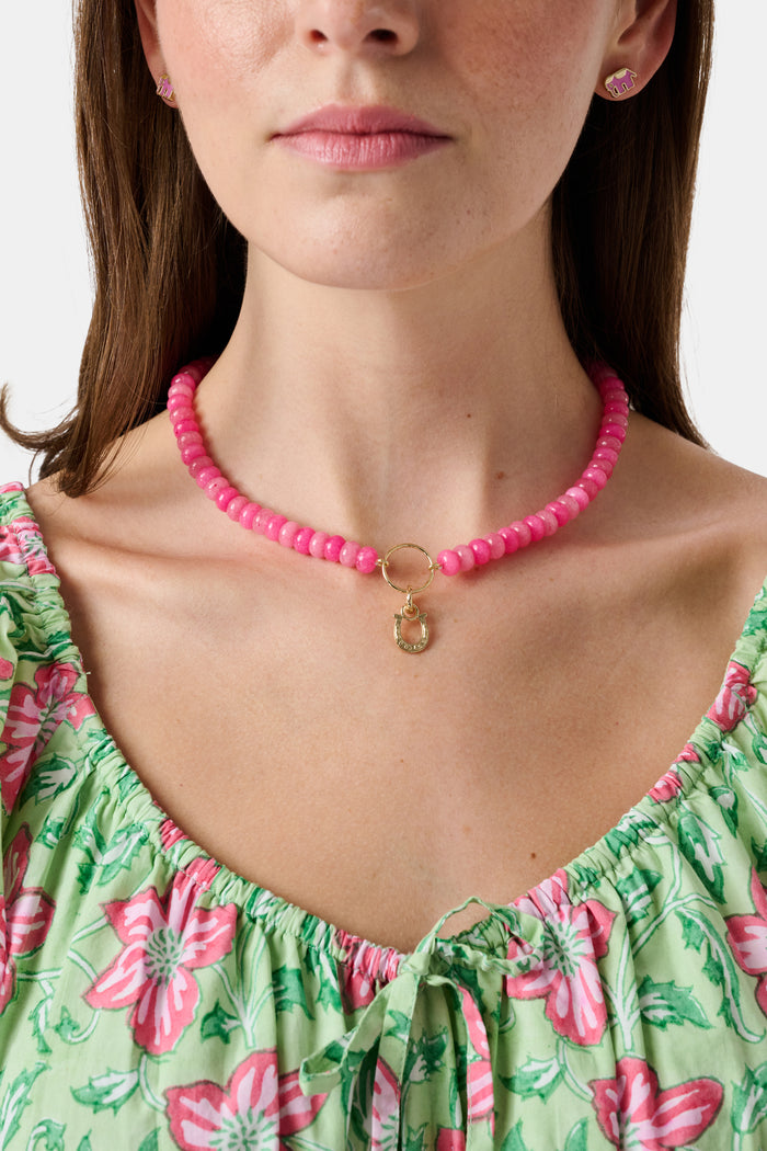 The Roller Rabbit Horseshoe Charm is a gold, horseshoe-shaped pendant designed as a luck charm, featuring a small loop at the top for attaching to a chain and set against a plain white background.