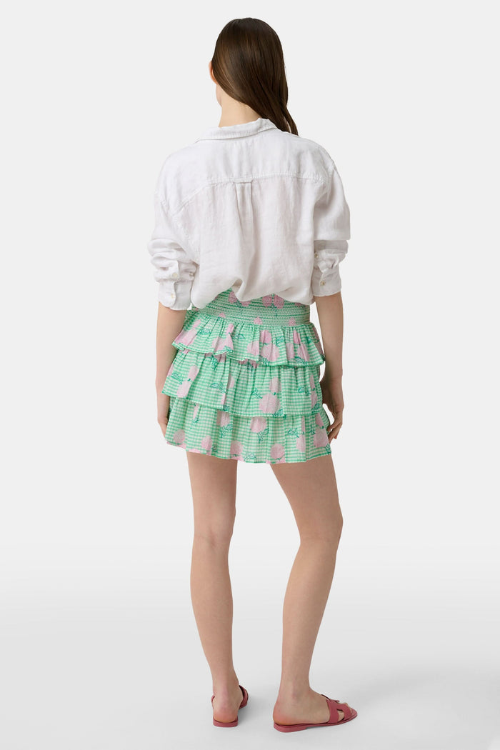 A person models the Roller Rabbit Hydrangea Gingham Siggy Skirt, featuring green and white checks with pink florals, paired with a tucked-in white shirt and red flat sandals. The image displays the skirt from waist to feet.