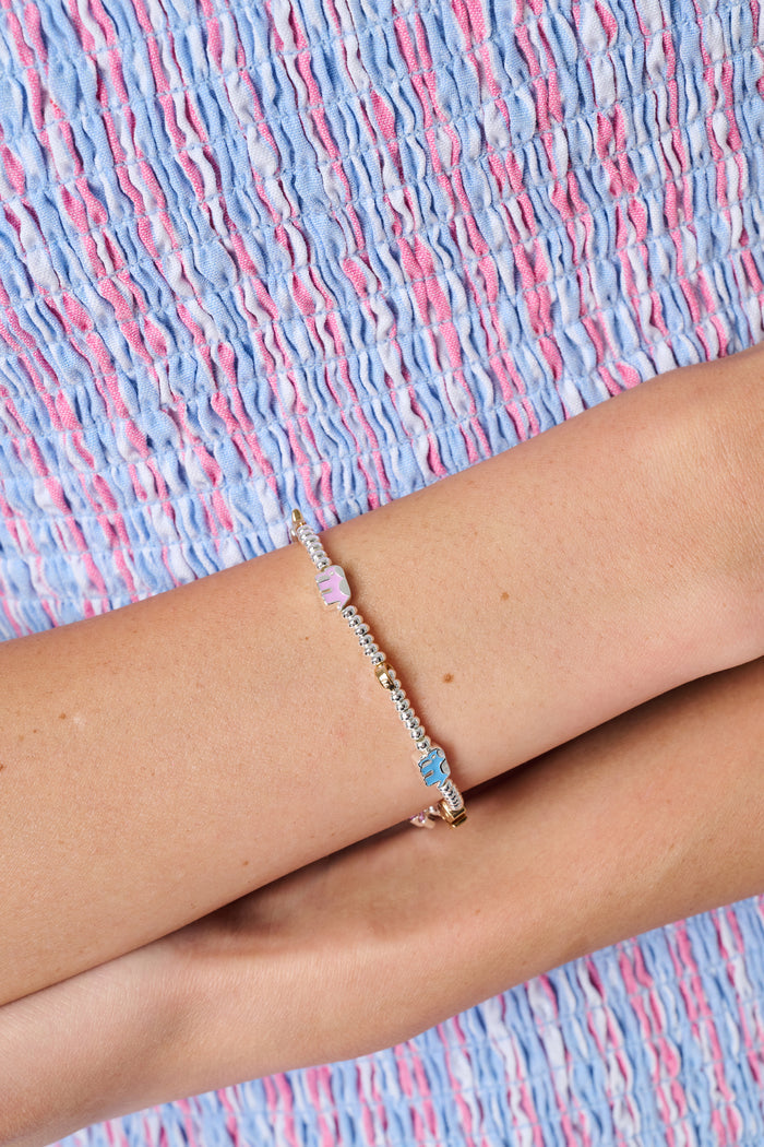 The Icon Party Beaded Bracelet by Roller Rabbit features a beaded silver chain adorned with colorful charms—including a pink monkey, blue elephant, yellow horseshoe, star, moon, and a blue eye—set against a white background.
