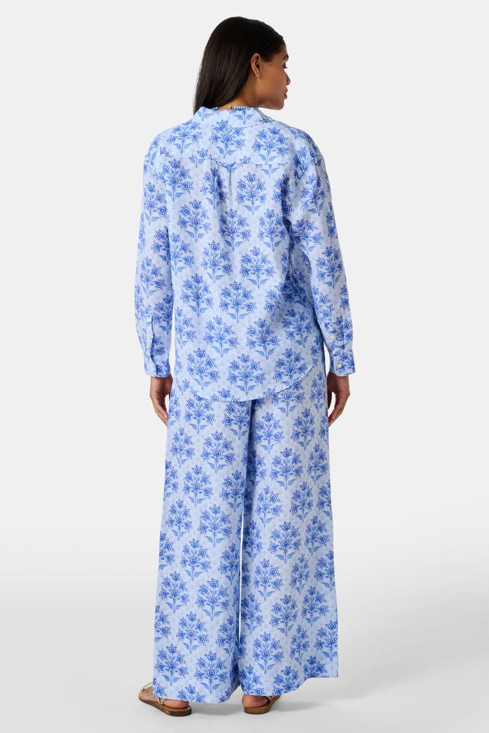 Close-up of the light blue Indigo Garden Paige Pant by Roller Rabbit, featuring a repeating pattern of darker blue floral designs and small star-like shapes. The fabric appears slightly wrinkled.