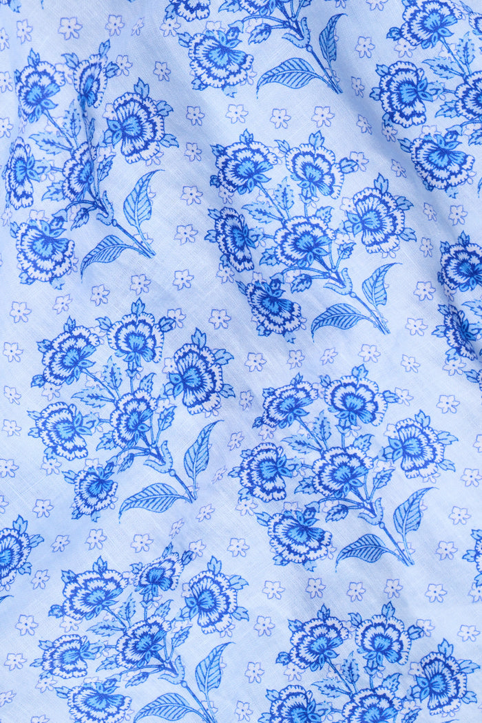 A woman stands against a plain light background wearing the Roller Rabbit Indigo Garden Boyfriend Shirt, a button-up long-sleeve pajama top in a blue floral print paired with matching wide-leg pants.