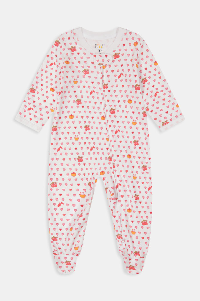 A woman in the Roller Rabbit Autumn Hearts Fiora Pajamas and brown boots sits on a wooden fence, smiling and resting one arm on a tree branch in a sunny outdoor setting, evoking the coziness of fall sleepwear.