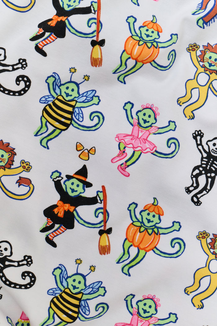 A smiling child in Roller Rabbit’s Kids Boo Crew Pajamas, crafted from soft Pima cotton, sits with arms raised on outdoor steps among women in coordinating patterned pajamas, all sharing a cheerful and relaxed moment together.