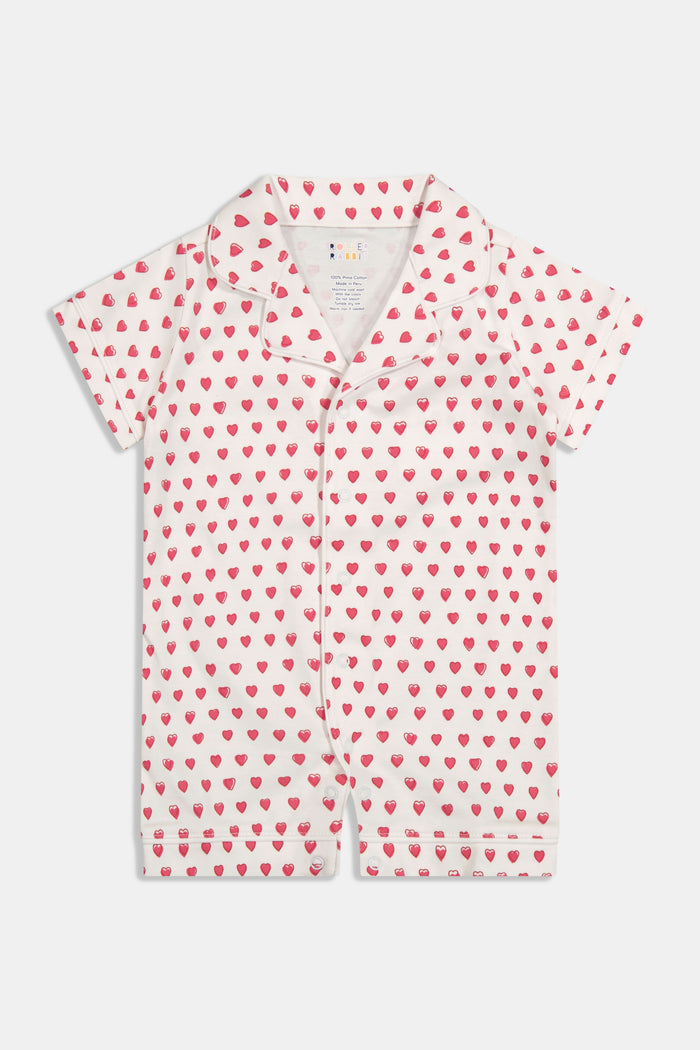 A baby with light skin and light brown hair lies on a pink and white striped blanket wearing the Roller Rabbit Infant Hearts Polo Onesie, looking slightly to the side.