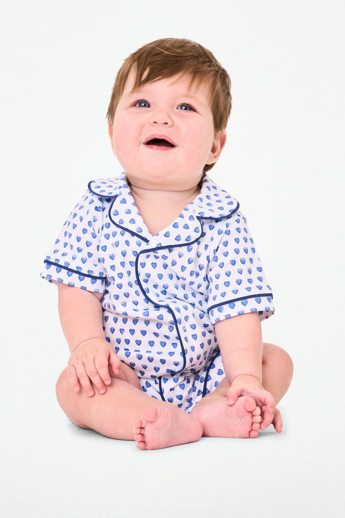The Infant Hearts Polo Onesie by Roller Rabbit features a blue heart print, navy piping, a button-up front, and classic collar—offering a look inspired by playful blue heart rompers.
