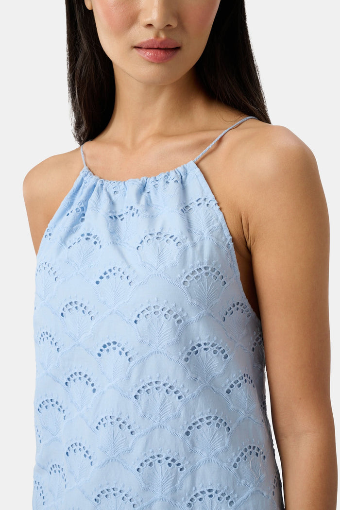 A woman wears the Roller Rabbit Jemina Eyelet Athena Dress, a sky blue, sleeveless cotton sundress with a gathered halter neckline and eyelet details, paired with white sandals, set against a plain white background.