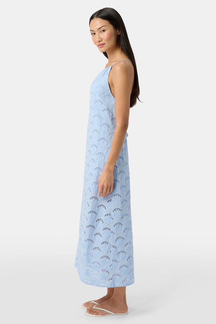 A woman wears the Roller Rabbit Jemina Eyelet Athena Dress, a sky blue, sleeveless cotton sundress with a gathered halter neckline and eyelet details, paired with white sandals, set against a plain white background.