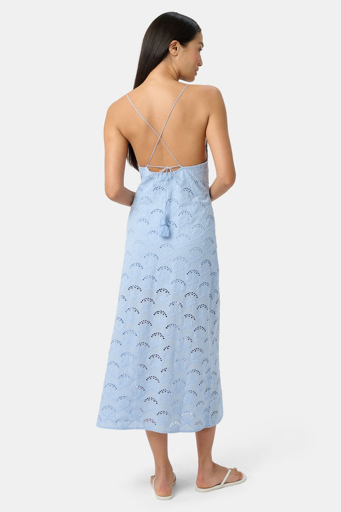 A woman wears the Roller Rabbit Jemina Eyelet Athena Dress, a sky blue, sleeveless cotton sundress with a gathered halter neckline and eyelet details, paired with white sandals, set against a plain white background.