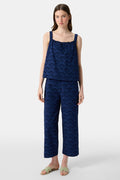 A woman with long brown hair wears the Roller Rabbit Jemina Eyelet Estelle Top in navy and wide-leg pants with a scalloped texture, paired with light green slide sandals. She stands against a plain white background.