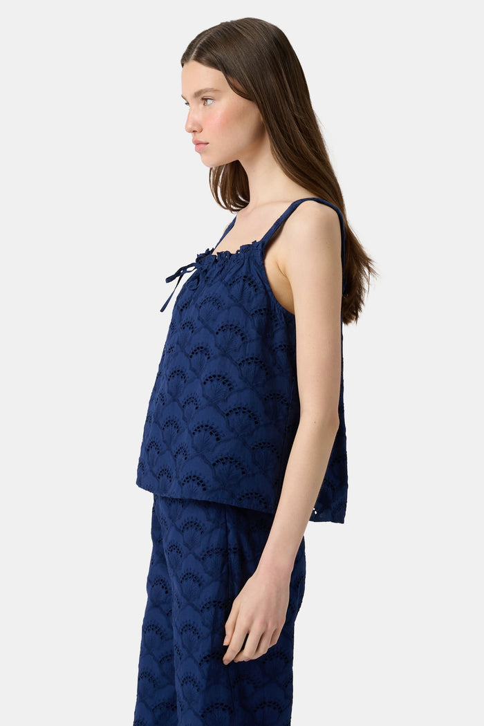 A woman with long brown hair wears the Roller Rabbit Jemina Eyelet Estelle Top in navy and wide-leg pants with a scalloped texture, paired with light green slide sandals. She stands against a plain white background.