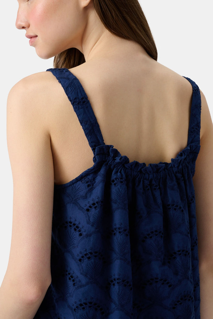 A woman with long brown hair wears the Roller Rabbit Jemina Eyelet Estelle Top in navy and wide-leg pants with a scalloped texture, paired with light green slide sandals. She stands against a plain white background.