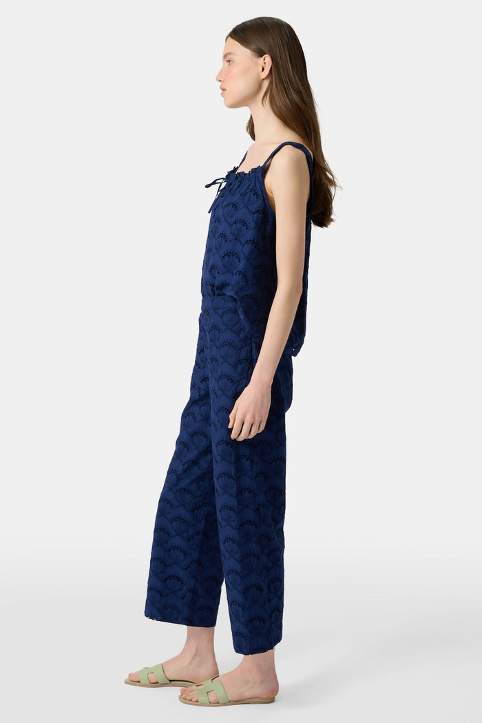 A person wearing Roller Rabbit's Jemina Eyelet Kendall Pant in navy blue, ankle-length, paired with light green slide sandals and standing against a plain white background.