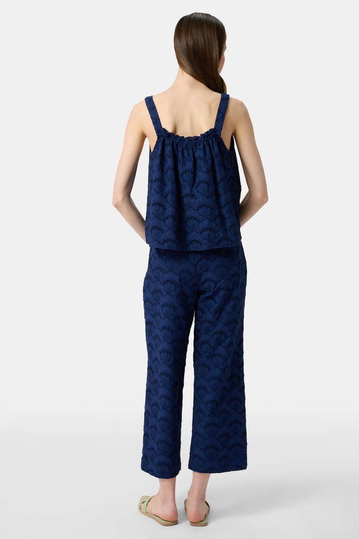 A person wearing Roller Rabbit's Jemina Eyelet Kendall Pant in navy blue, ankle-length, paired with light green slide sandals and standing against a plain white background.