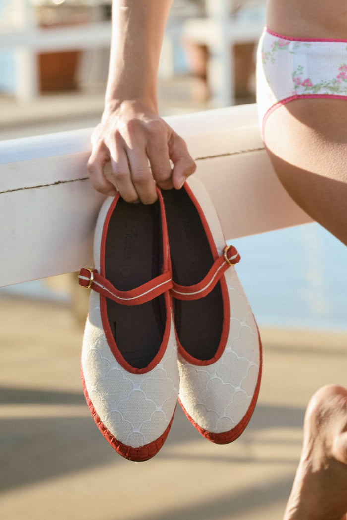 The Jena Embroidery Pierre by FLABELUS is a beige Mary Jane shoe, handmade in Spain, with a white pattern, red trim, a red strap and gold buckle, plus a black sole.