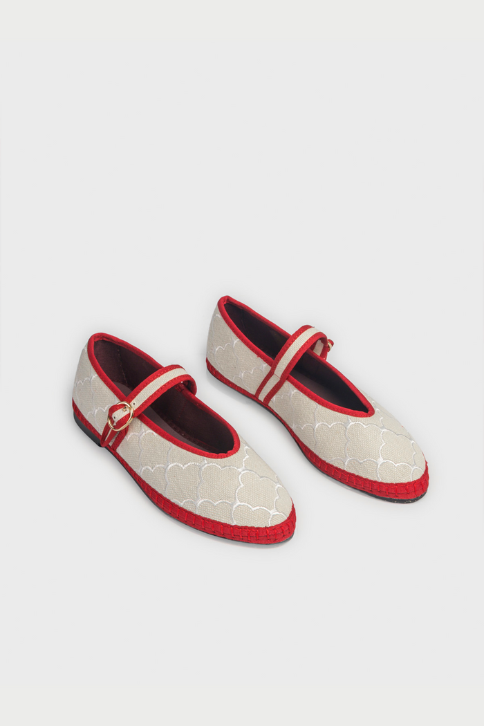 The Jena Embroidery Pierre by FLABELUS is a beige Mary Jane shoe, handmade in Spain, with a white pattern, red trim, a red strap and gold buckle, plus a black sole.