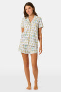 The Kappa Alpha Theta Monkey Polo Pajamas from Roller Rabbit are a short-sleeve button-up set with matching shorts, showcasing a lively print of colorful cartoon monkeys and doodles on a crisp white background. They feature an elastic waistband for comfort and are crafted from soft Pima cotton for a gentle feel.